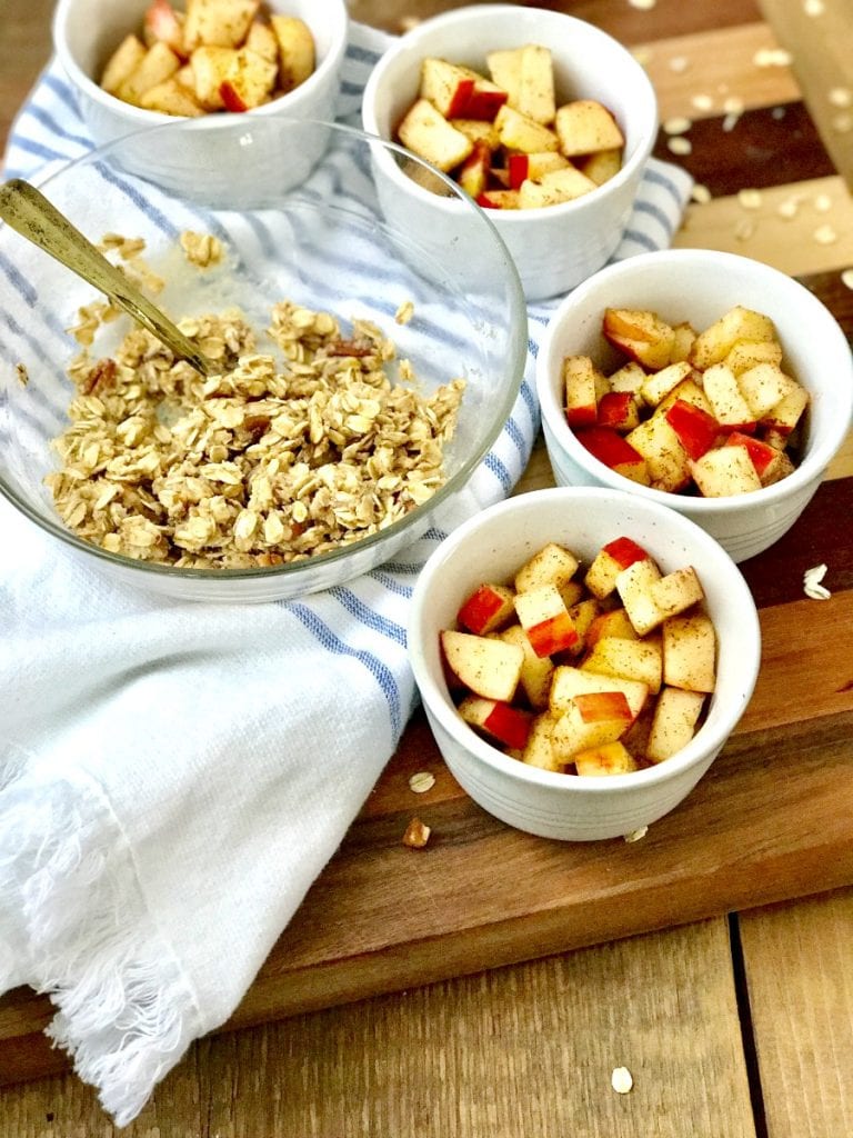 Apples in ramekins with a crisp topping sitting nearby 