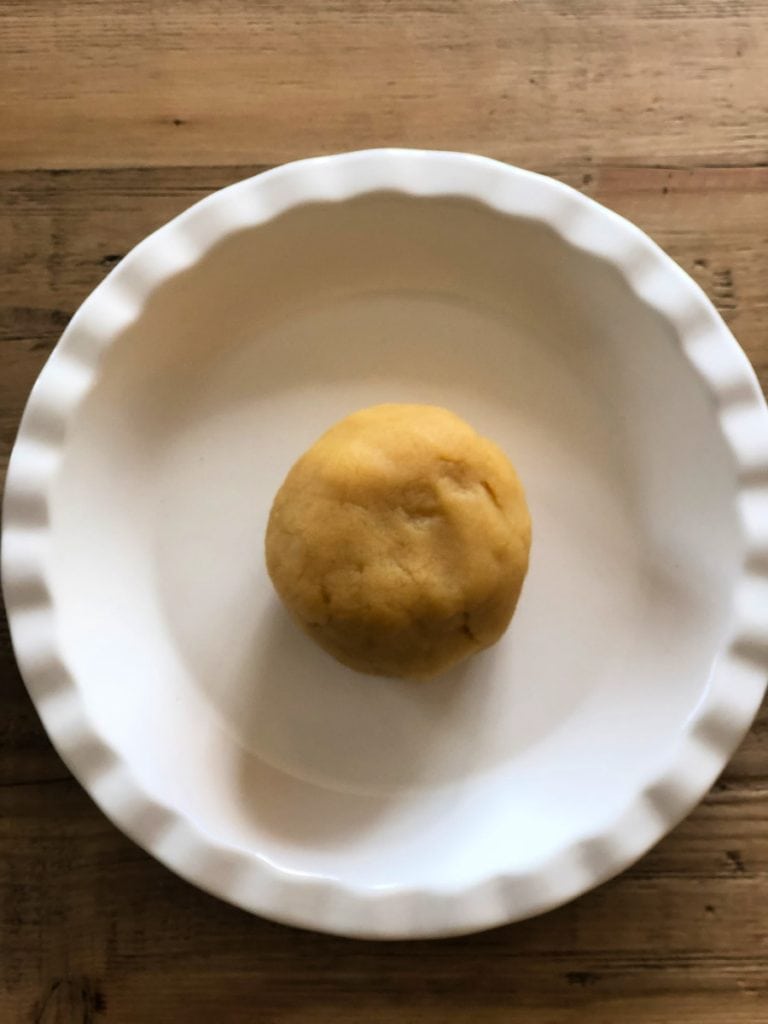 Almond Flour pie crust in a ball in the center of a pie plate on a wooden background