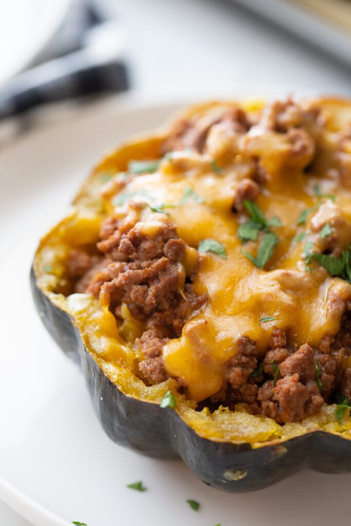 Taco stuffed acorn squash topped with cheese and cilantro on a white plate.