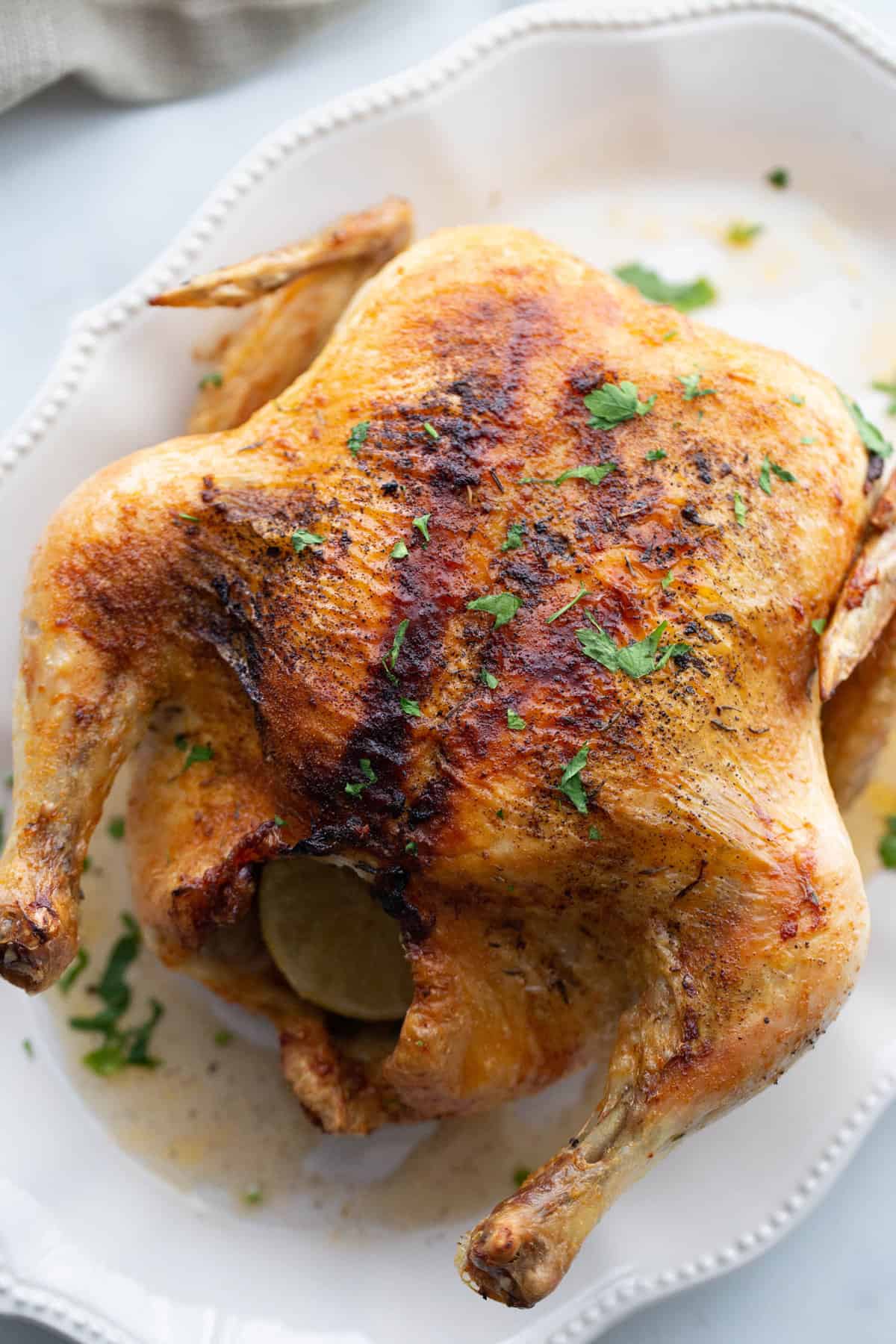 Air fryer whole chicken on a white platter before carving.