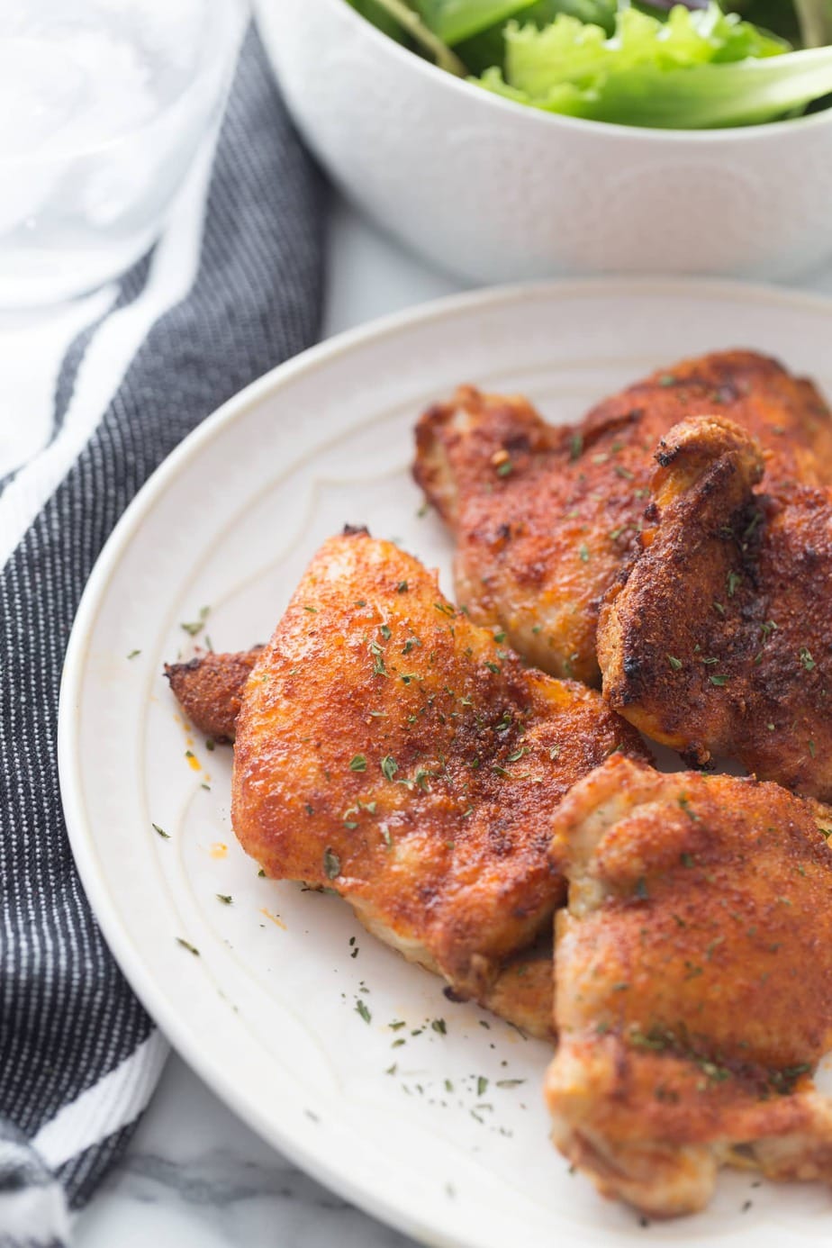 Overlapping pieces of air fryer chicken thighs on white plate. 