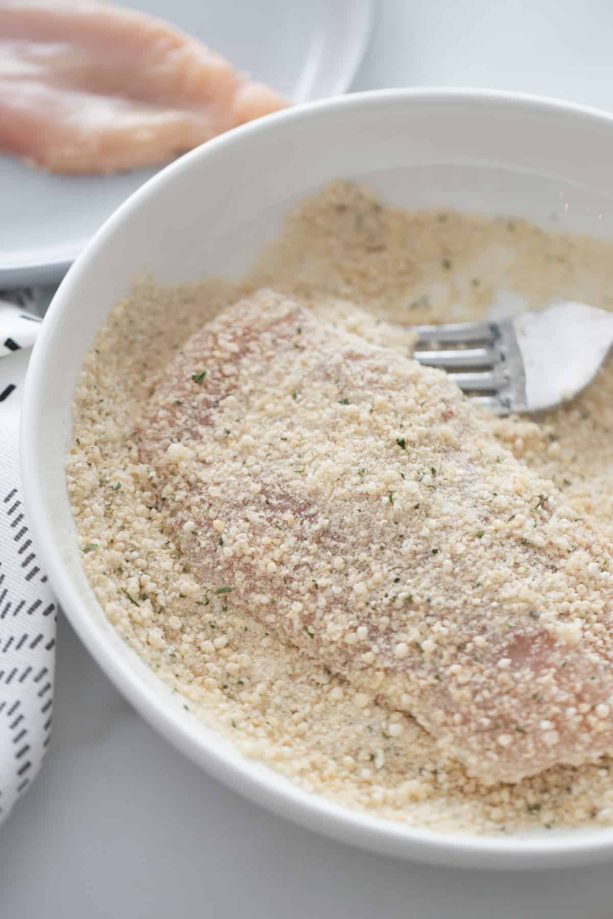 Breading a piece of chicken breast in a bowl of gluten free breadcrumbs