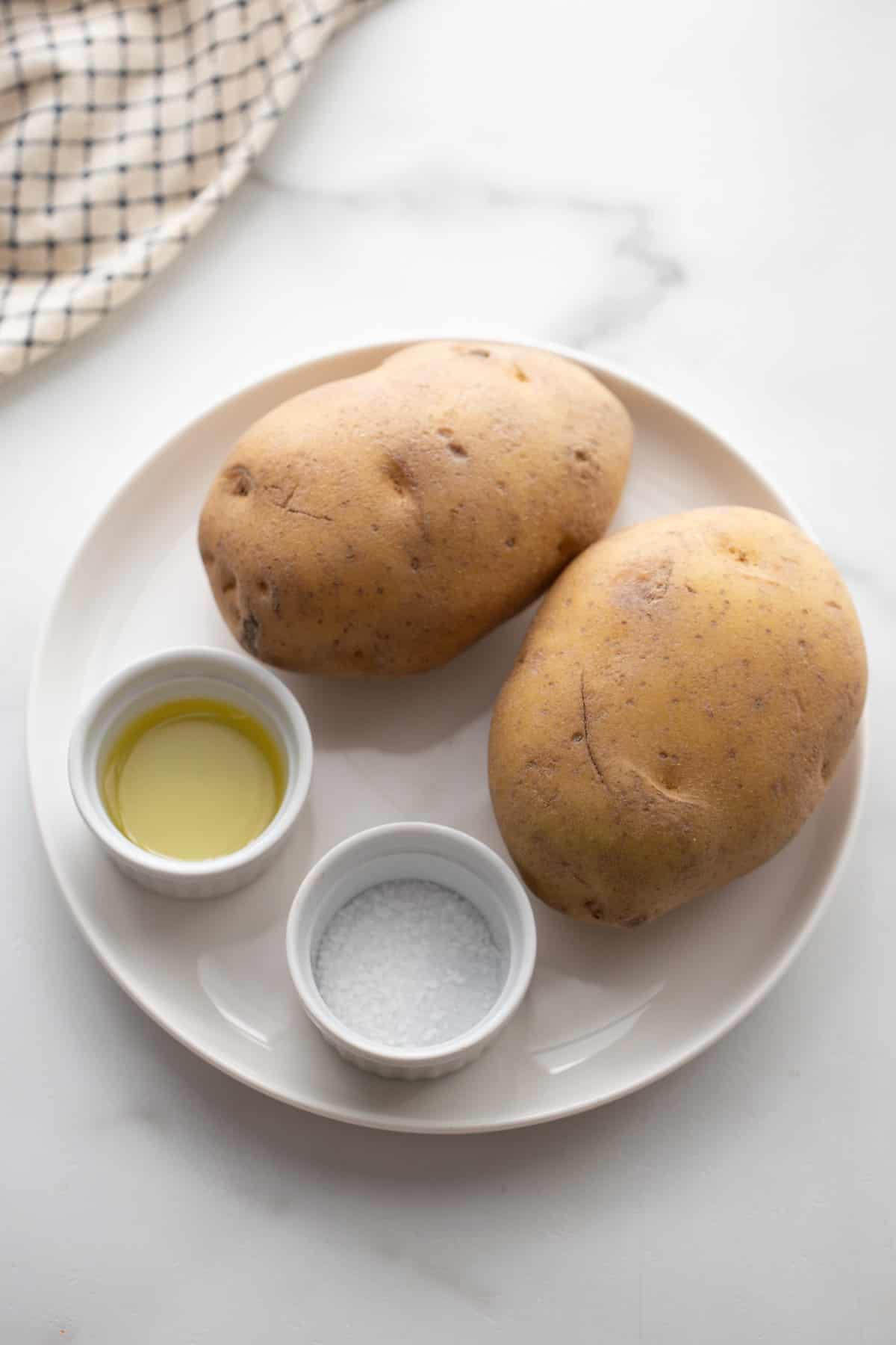 2 large raw potatoes, oil, and salt on a white dish - ingredients for homemade air fryer chips