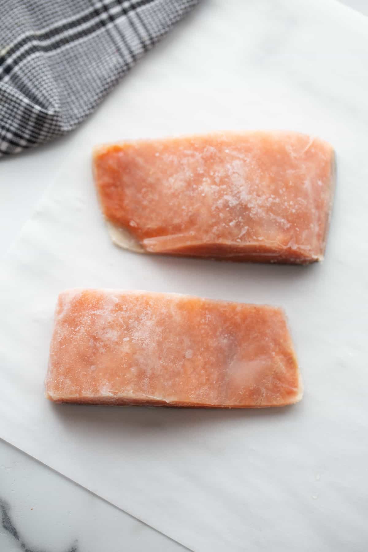 Two frozen salmon fillets on parchment paper. 