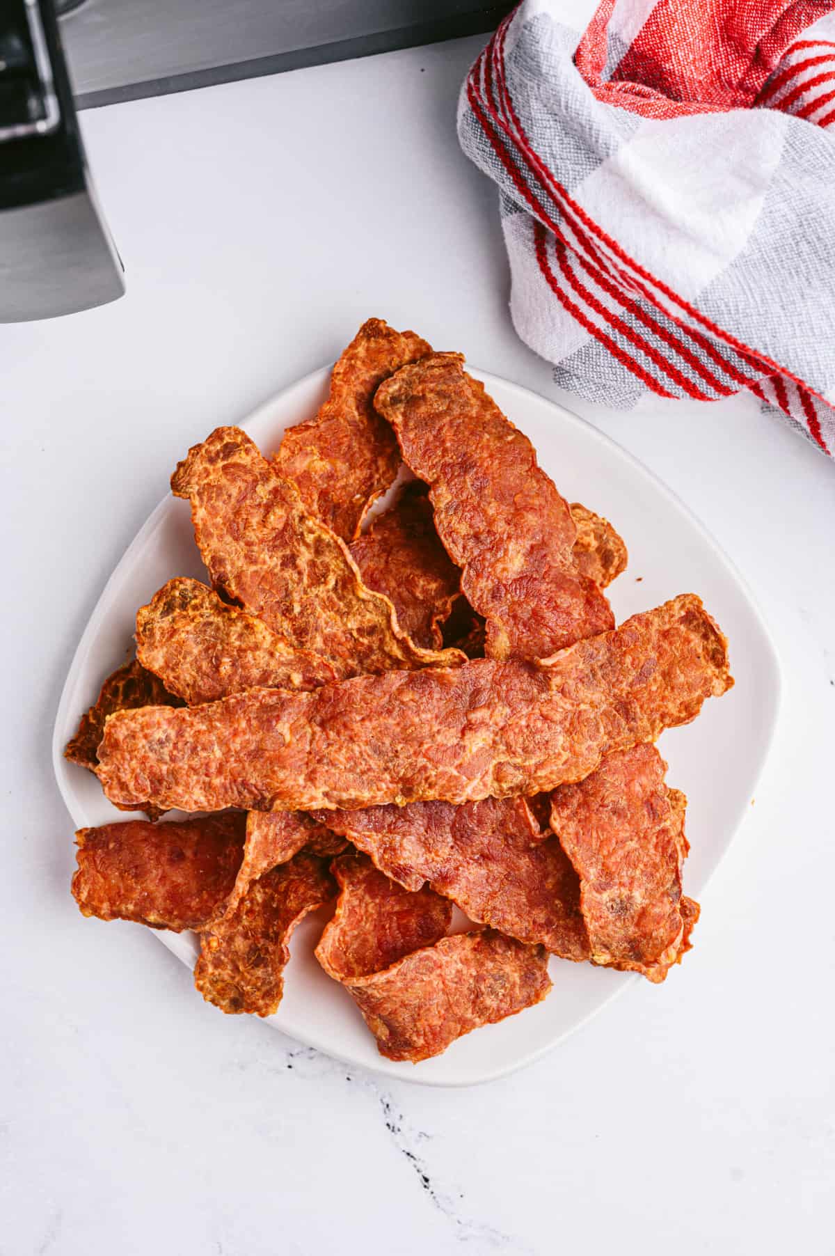 A plate of crispy turkey bacon on a white marble surface. 