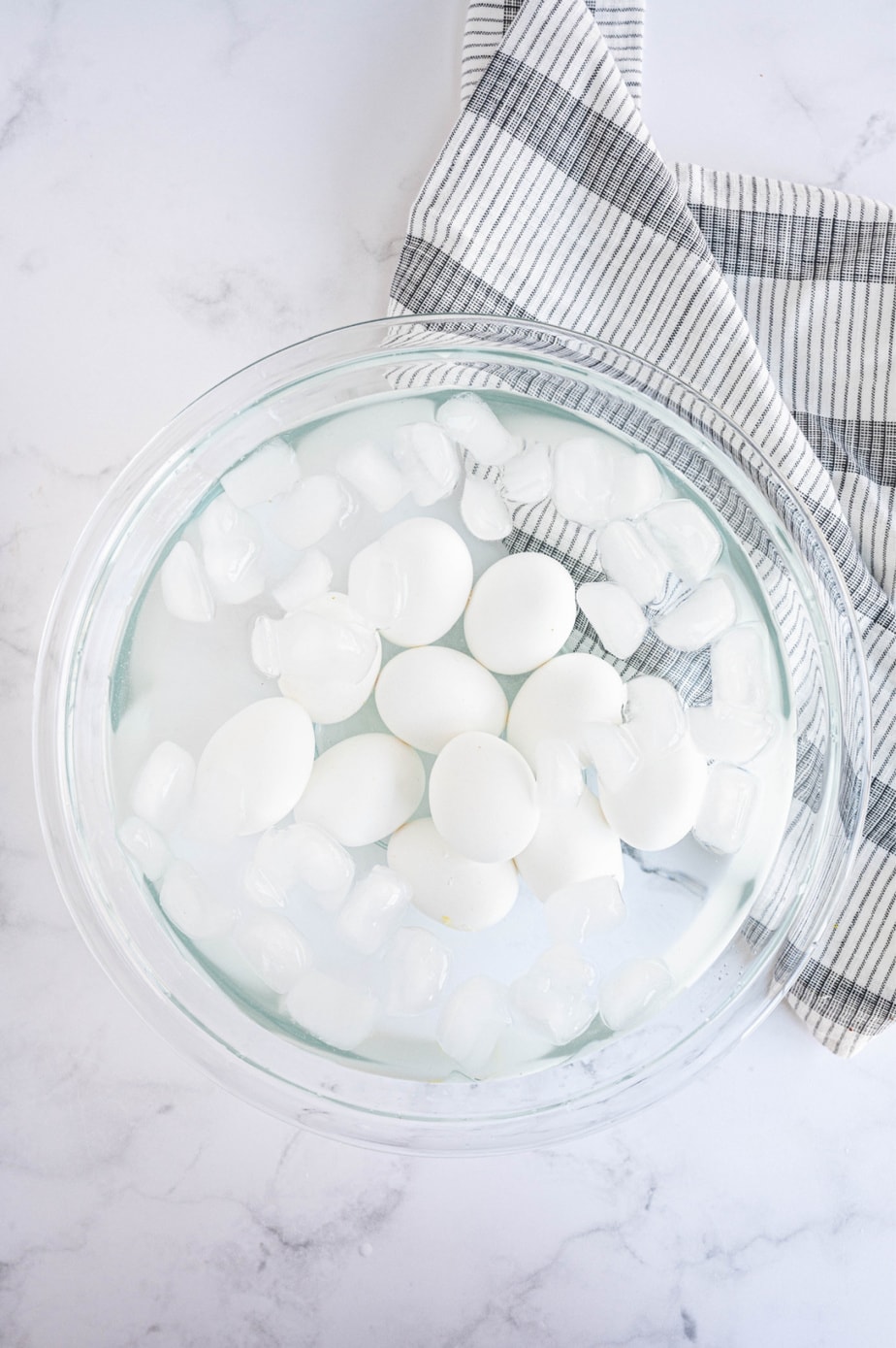 Cooked eggs are in a large glass bowl filled with ice and water.