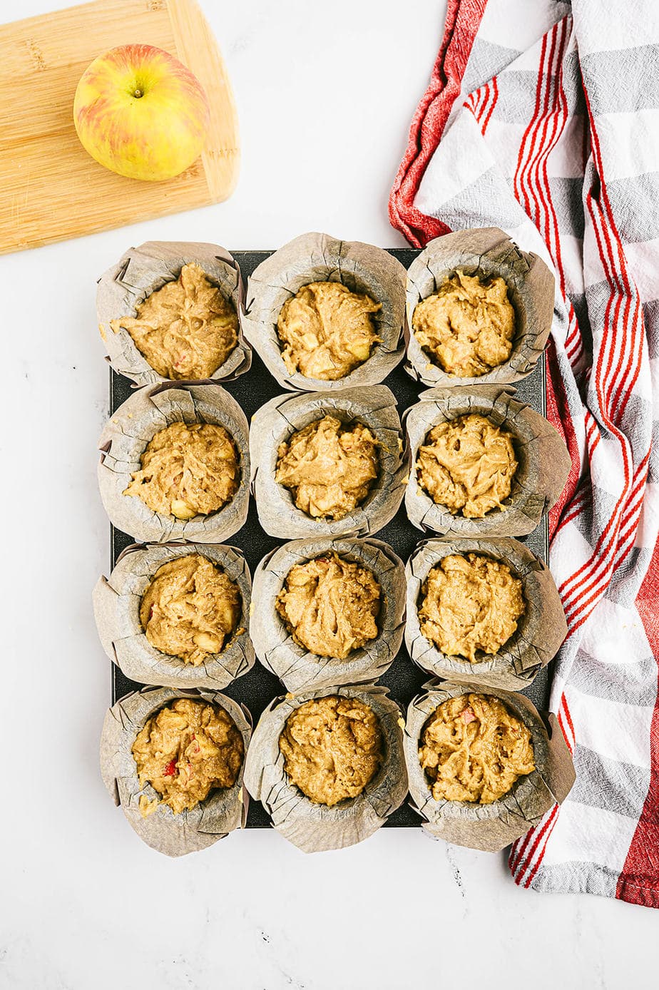 Overhead image: muffin tin full of apple muffin batter, ready for the oven