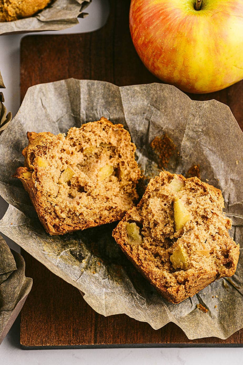 Close up photo of apple muffin, cut in half, laying on parchment liner.