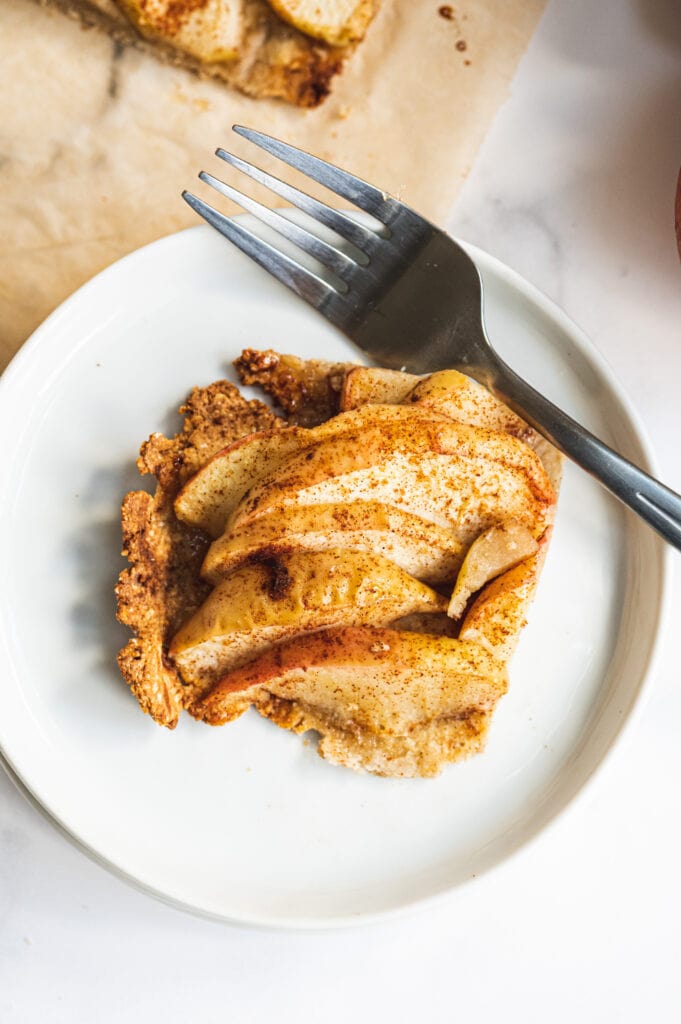 Overhead photo of a square of apple tart on a white plate with a fork poised on the side.