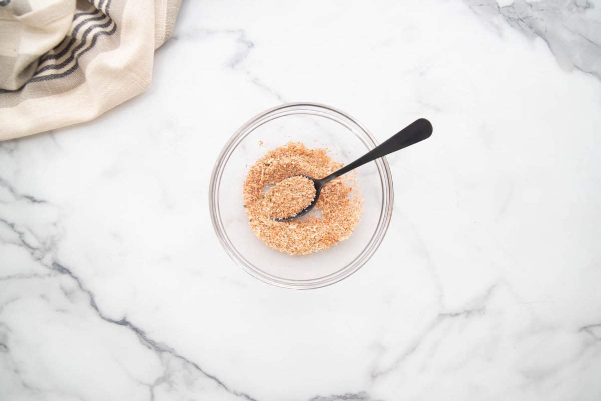 Parmesan cheese and dried seasonings in a small glass bowl with a black spoon.