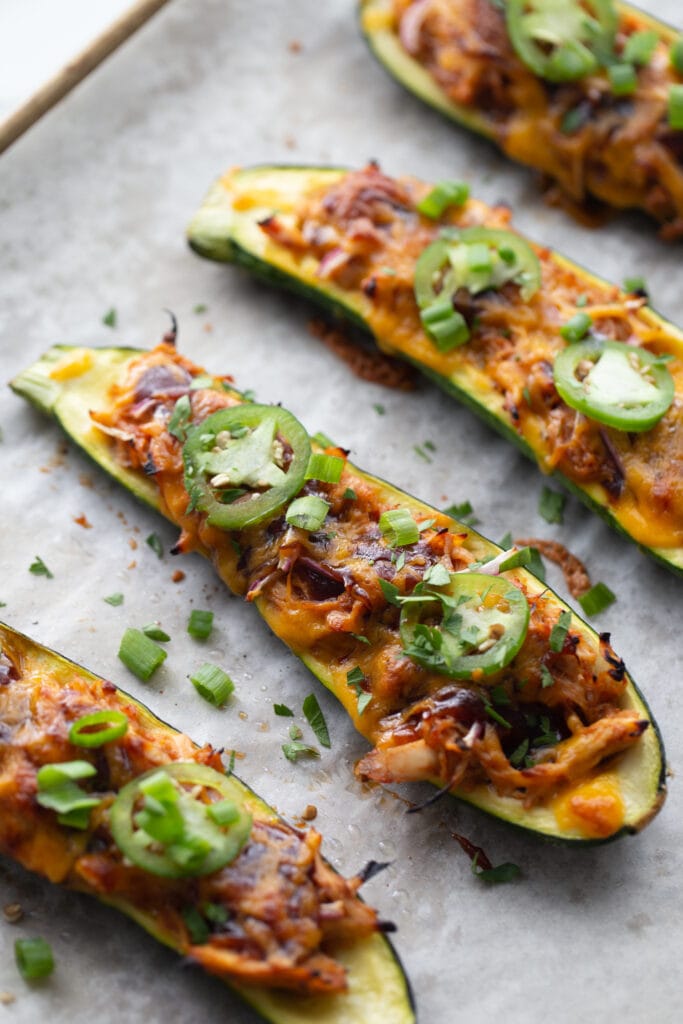 Overhead image: halved bbq chicken stuffed zucchinis on a parchment lined sheet pan