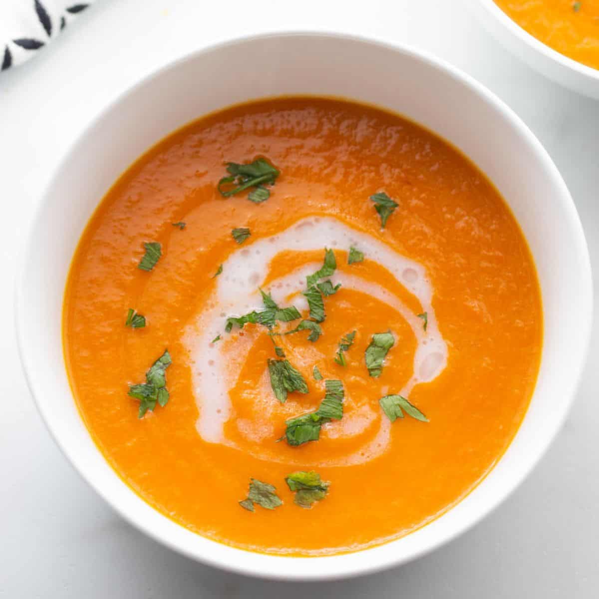 Two bowls of carrot ginger soup with a drizzle of coconut milk and a garnish of fresh parsley. 