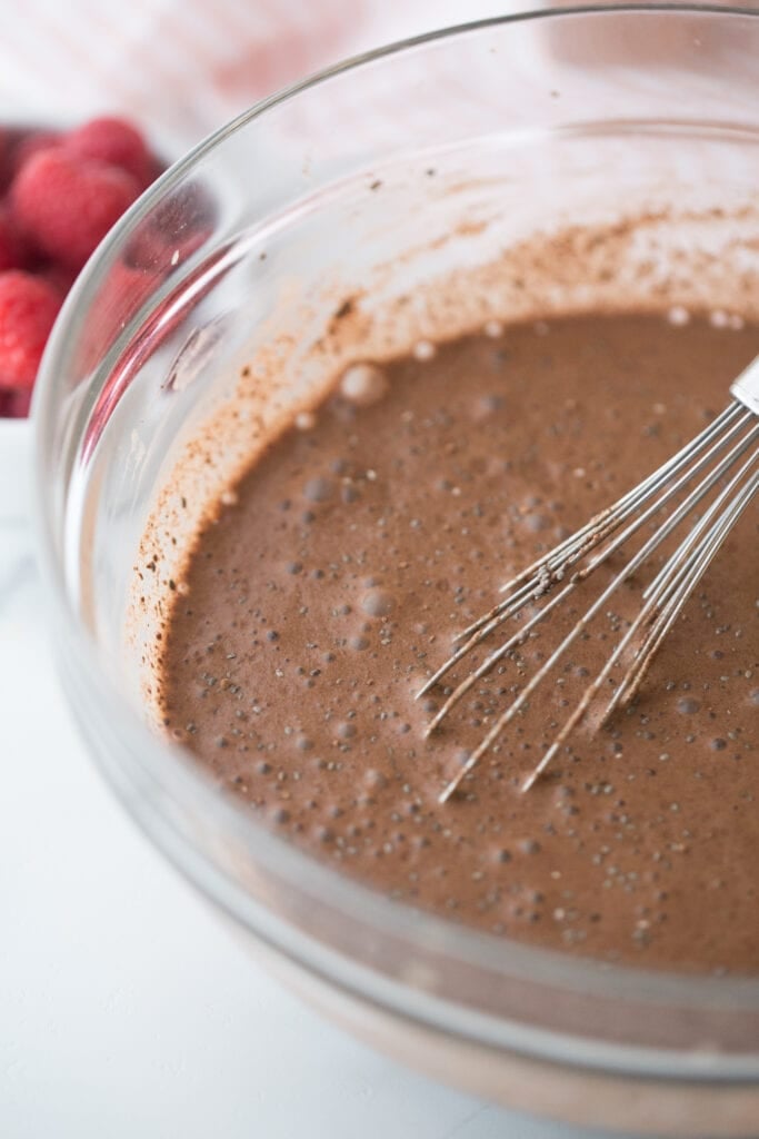 Close up photo of glass bowl full of chocolate chia pudding and a whisk, before being chilled