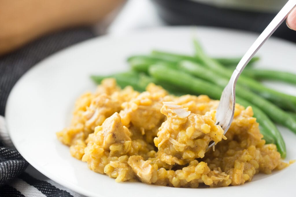 Close up side view of Instant Pot chicken curry with rice with a side of green beans. A person's hand is holding a fork is in the curry, ready for a bite!