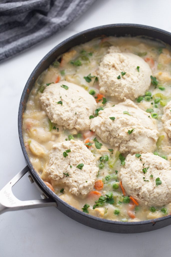 Overhead view of a healthy chicken pot pie in a skillet. It has a homemade biscuit topping and has fresh parsley as a garnish. 