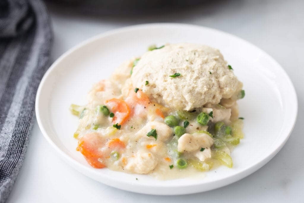 A hero shot of Gluten Free Chicken Pot pie on a white place with a grey striped napkin sitting to the left side. 