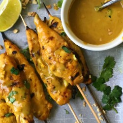 Chicken Satay Skewers on a Baking Pan with Creamy peanut sauce, crushed peanuts, and lime wedges