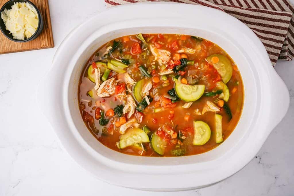 White crockpot of full of homemade chicken and vegetable soup.