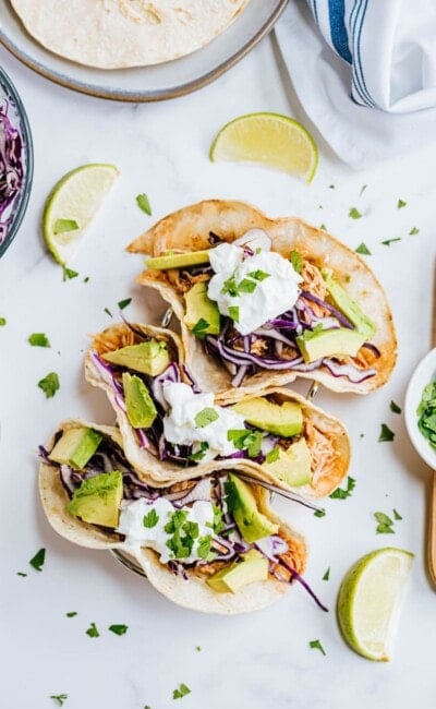 Three chicken tacos are garnished with cilantro and greek yogurt.