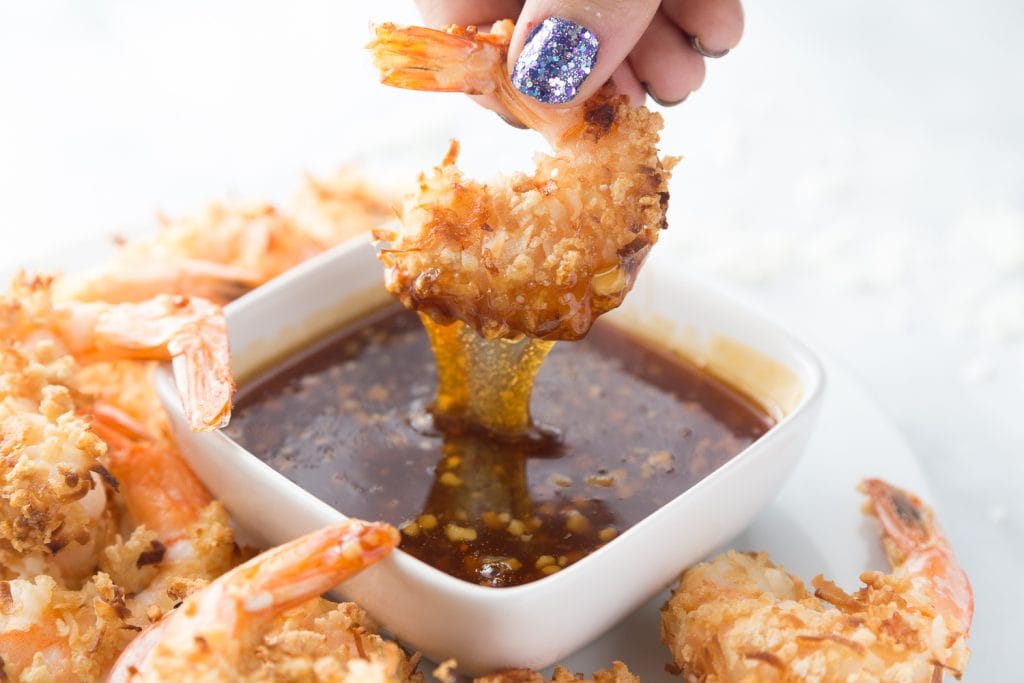 Close up of a coconut shrimp being dipped into a homemade sweet chili sauce 