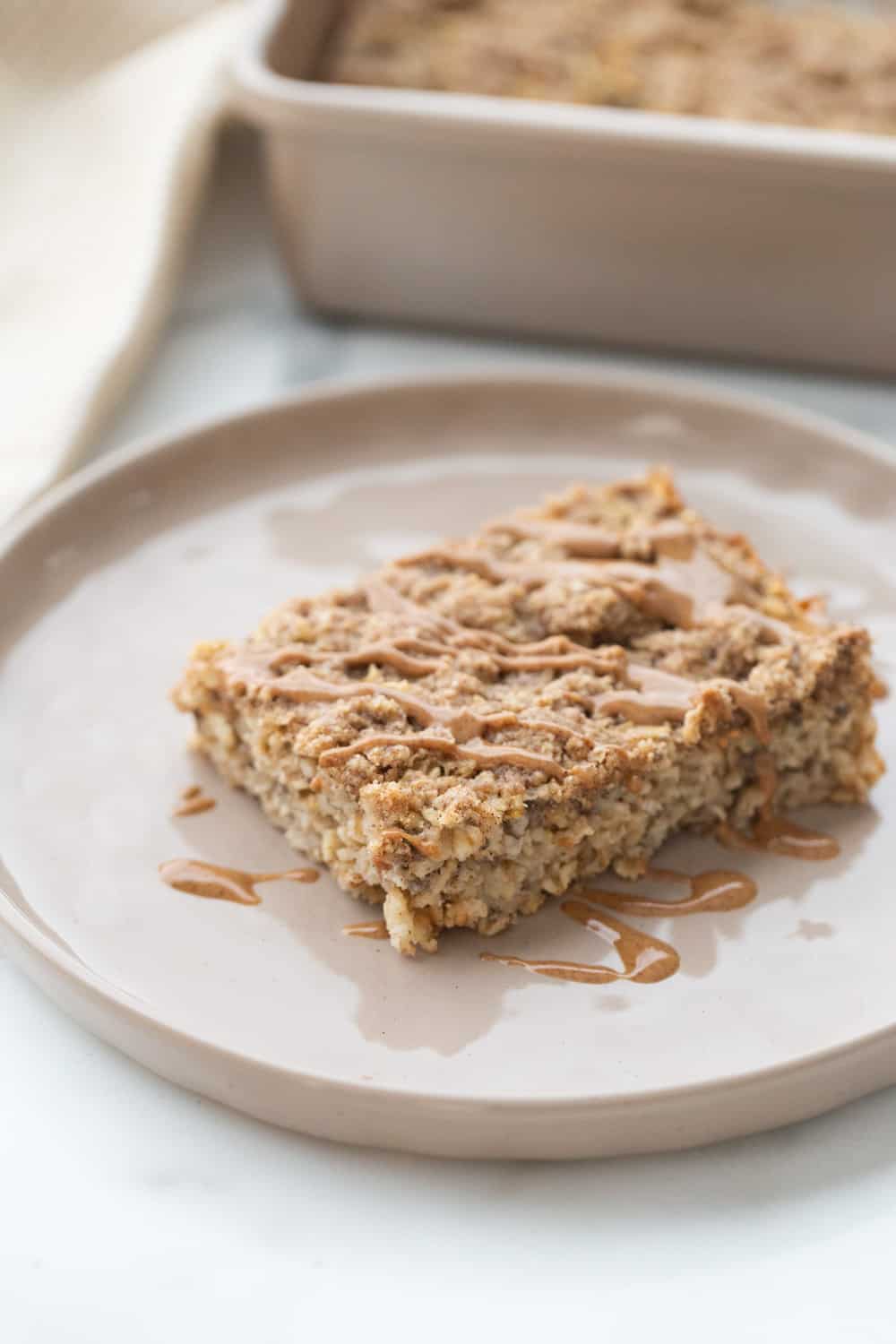 A piece of coffee cake baked oatmeal on a rimmed plate drizzled with peanut butter.