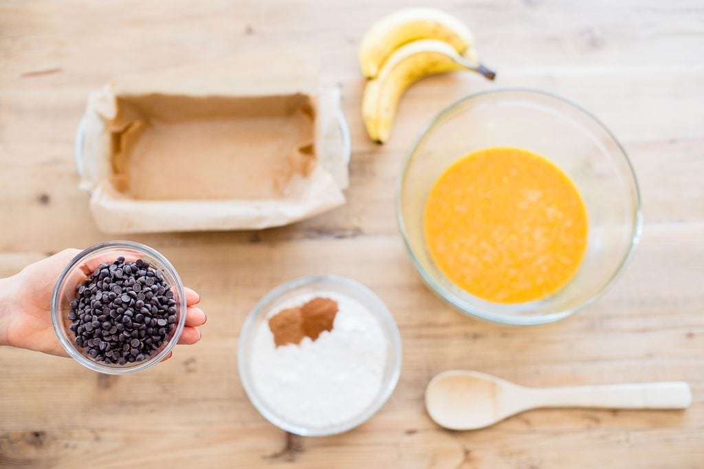 A flatlay of the ingredients to make Pumpkin Oatmeal Banana Bread on a light wood table. 