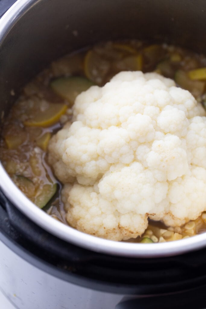 A head of whole cauliflower laying in a pot of corn chowder, ready to be blended.