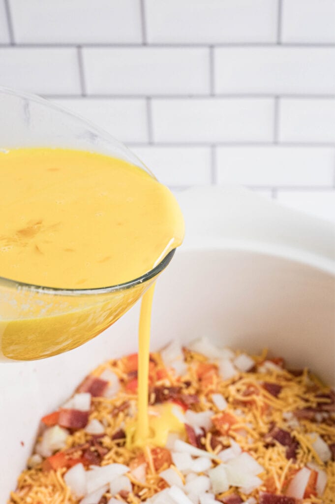 Pouring eggs over veggies and cheese in a slow cooker