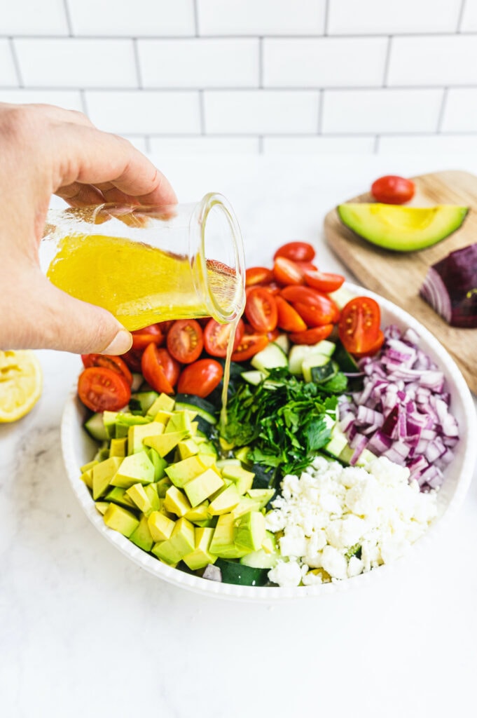 Dressing being poured on a cucumber tomato feta salad before mixing the ingredients.