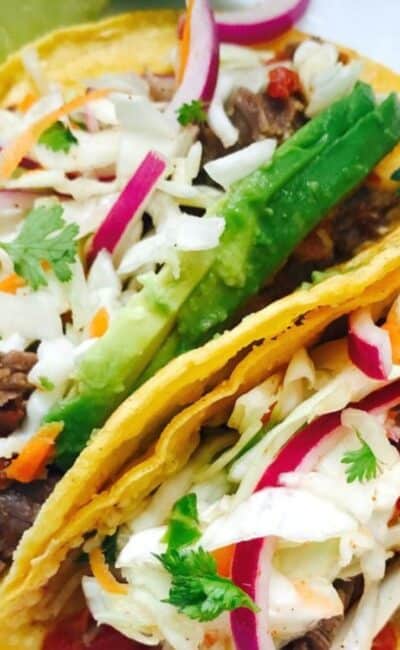 Close up of two flank steak tacos with cilantro lime slaw in corn tortillas.