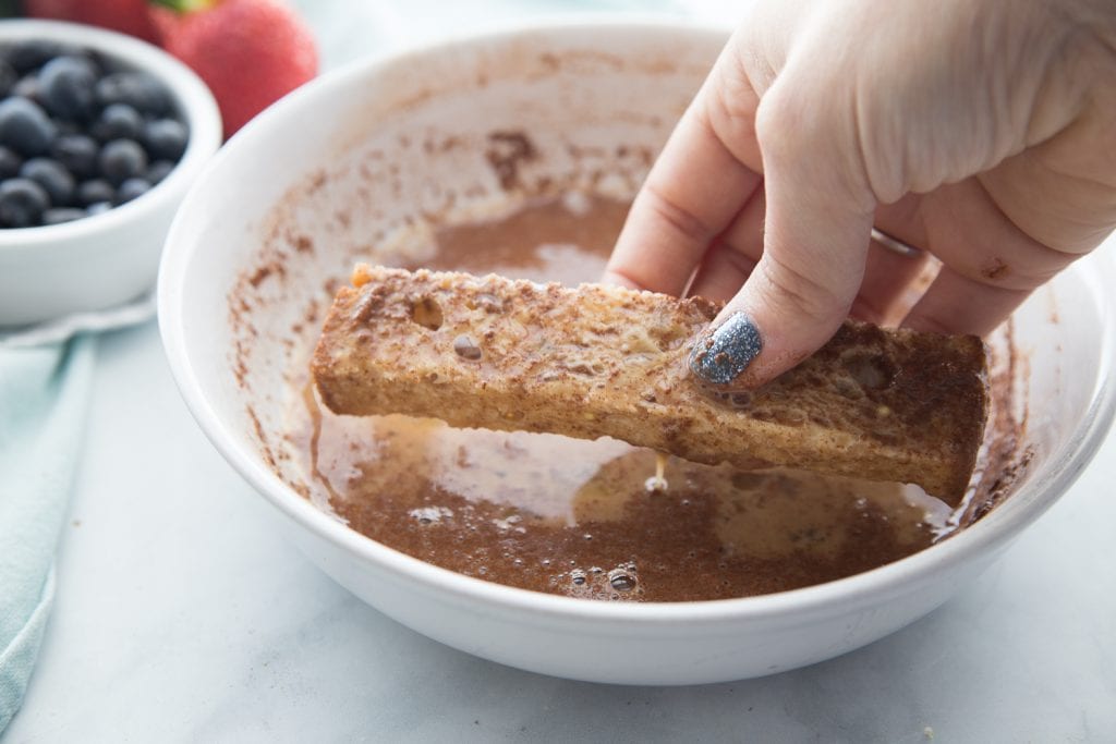 A french toast stick is being dipped in an egg mixture