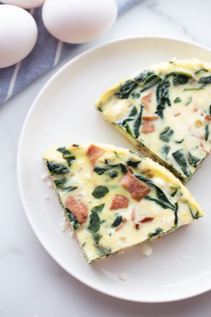 overhead closeup: two slices of bacon cheese egg frittata on white plate