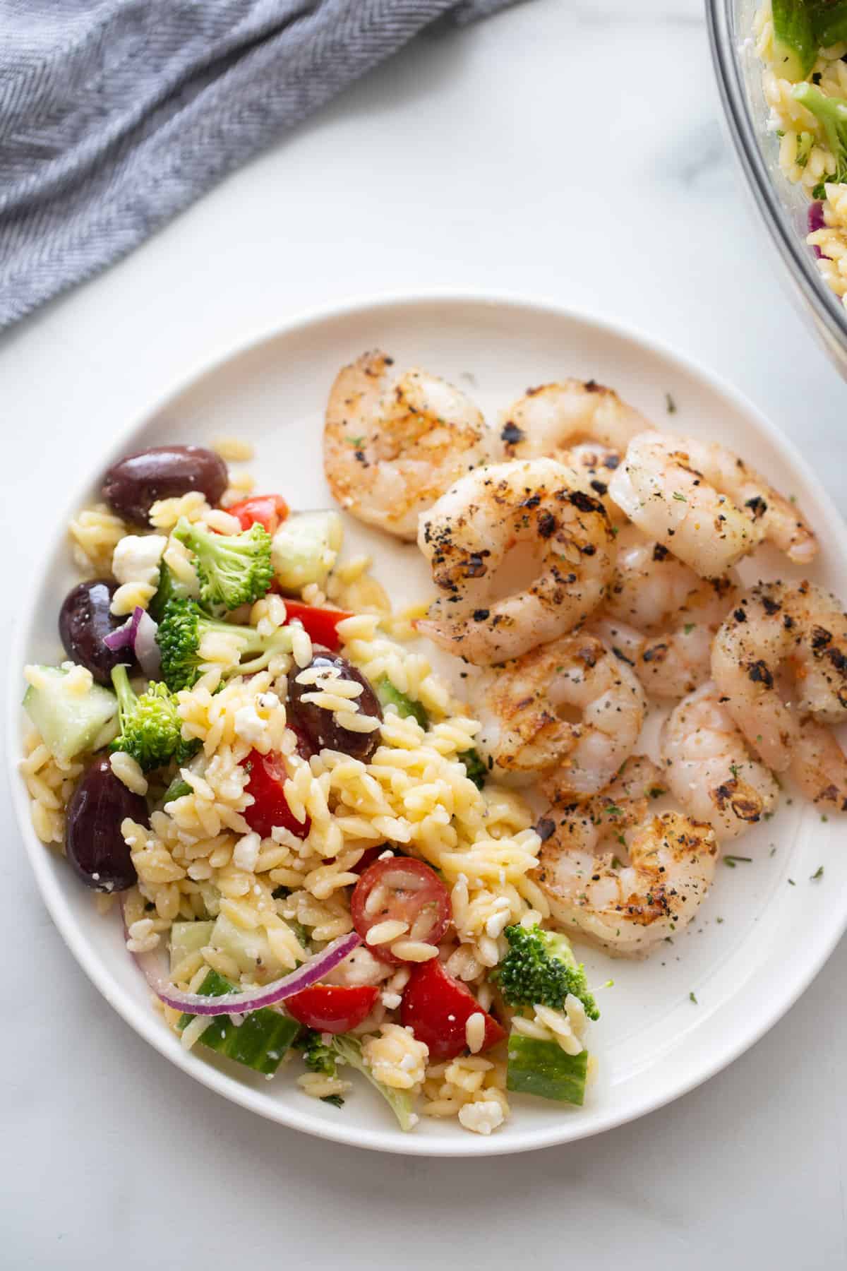 Overhead image of a round white plate half filled with grilled shrimp, half filled with orzo salad.