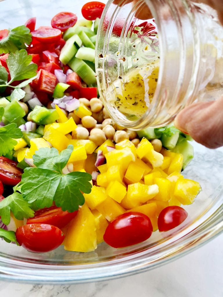 Homemade Greek dressing being poured over chickpeas and veggies for a 21 Day Fix Greek Salad