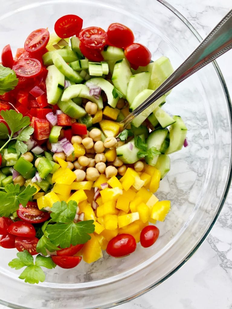 Lots of colorful veggies in a bowl with Chickpeas getting ready to make a Greek Chickpea Salad. 