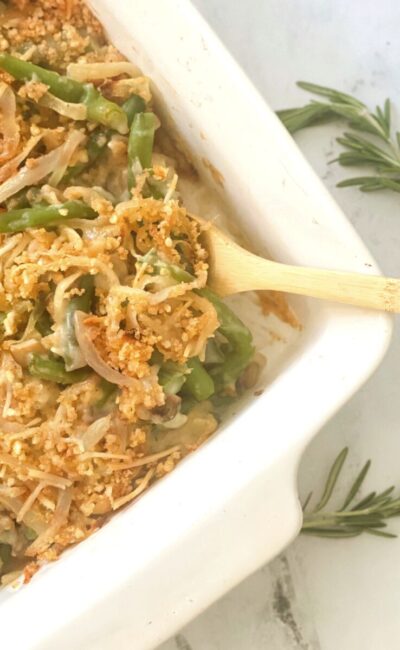Overhead image: green bean casserole with crispy onion topping in a white casserole dish with a wooden spoon.