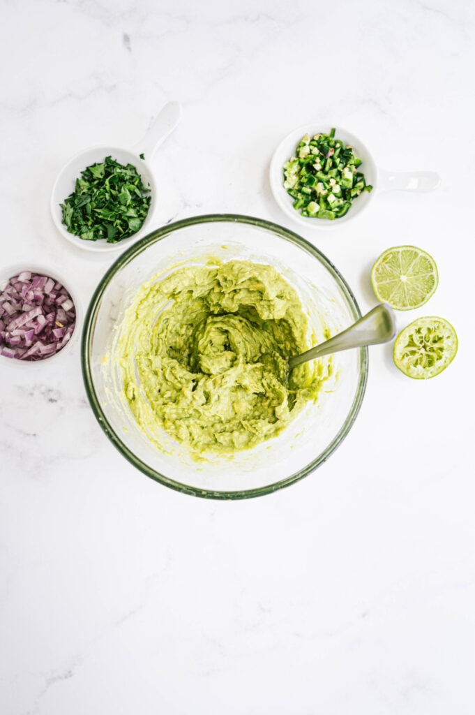 Ingredients for chipotle guacamole on a white marble table in small bowls ready to be mixed 