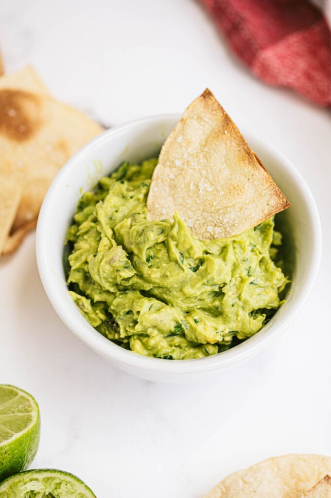 An overhead shot of guacamole with a homemade corn tortilla chip dipped inside 