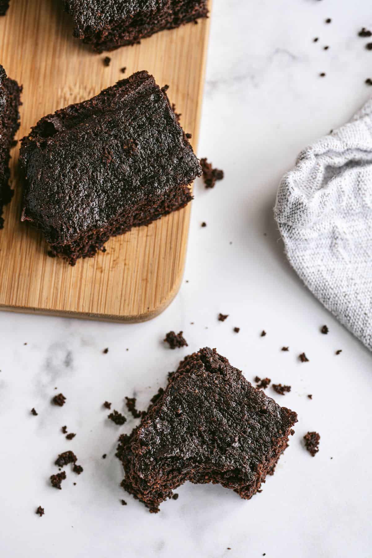 Homemade brownies on a wooden cutting board and marble countertop with brownie crumbs scattered around.