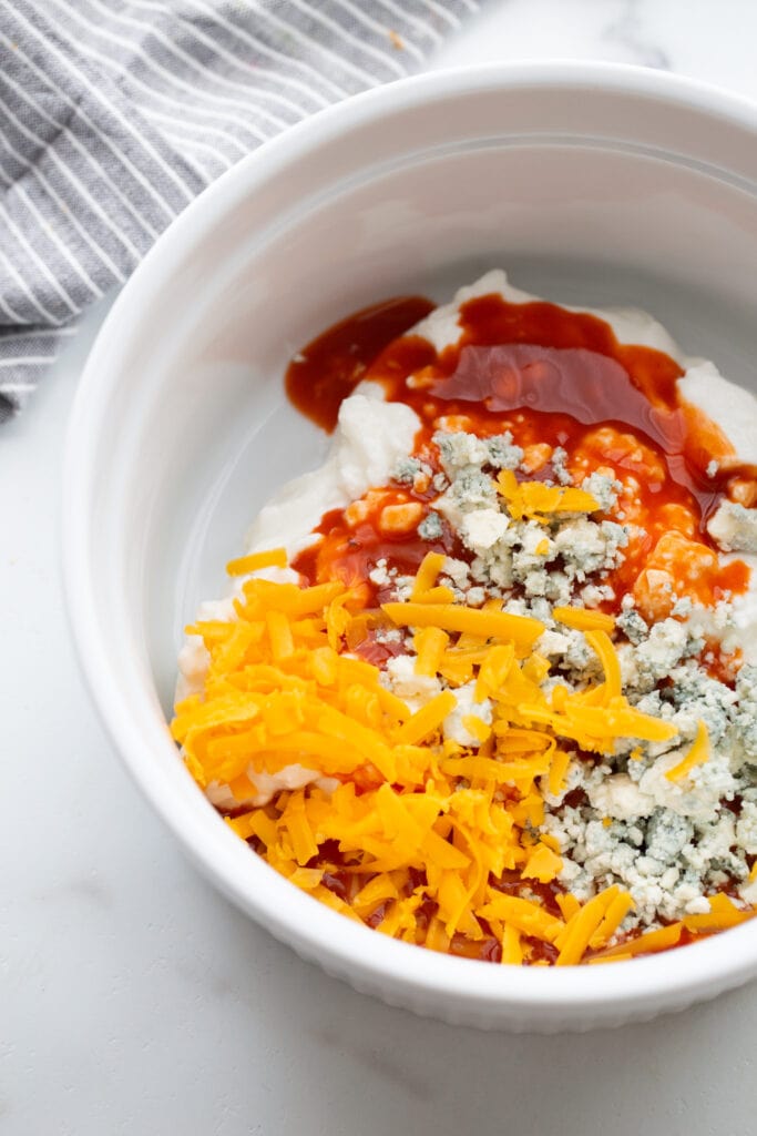 Casserole dish filled with cottage cheese, blue cheese, cheddar cheese, and hot sauce, ready to be mixed.