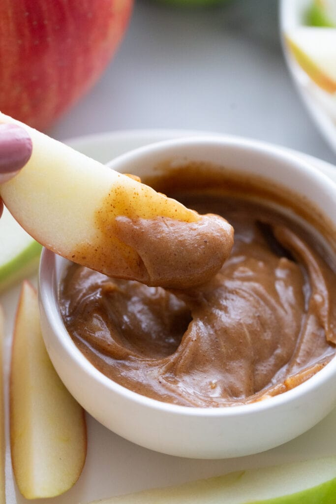 Apple slice dipped in a small bowl of homemade caramel 