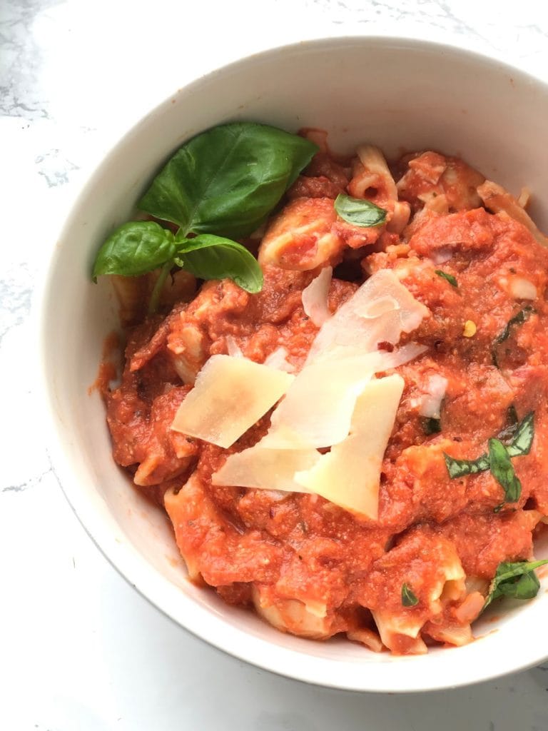 A close up shot of a bowl of healthy penne vodka with chicken topped with parmesan cheese