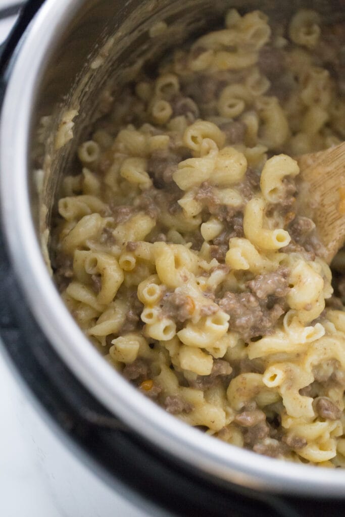 Close up overhead view of healthy hamburger helper ready to be eaten! There is a wooden spoon to the right side of the image stirring the pasta, cheese, and hamburger meat.