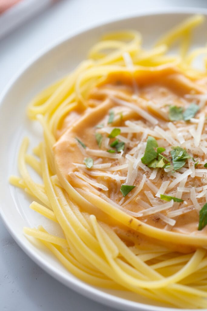 High angle close up photo of fettuccine topped with pumpkin alfredo sauce, shredded cheese and parsley.