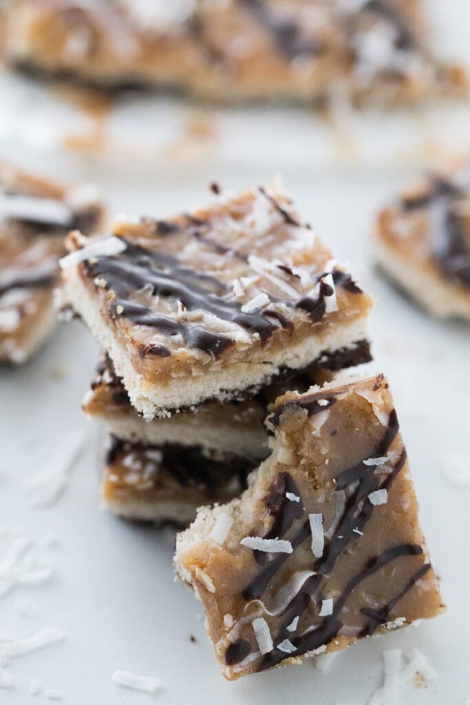 Close up of a stack of Healthy Samoas Cookie Bars. There is one leaning against the stack, and more in the background out of focus.