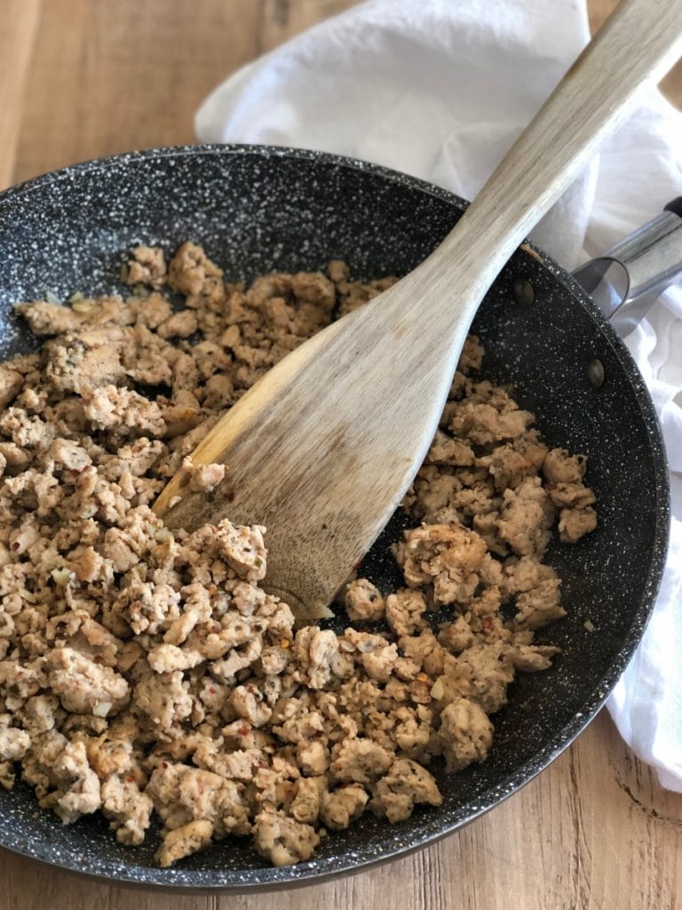 A pan of homemade chicken sausage sitting on top of a wooden table with a wooden spatula inside