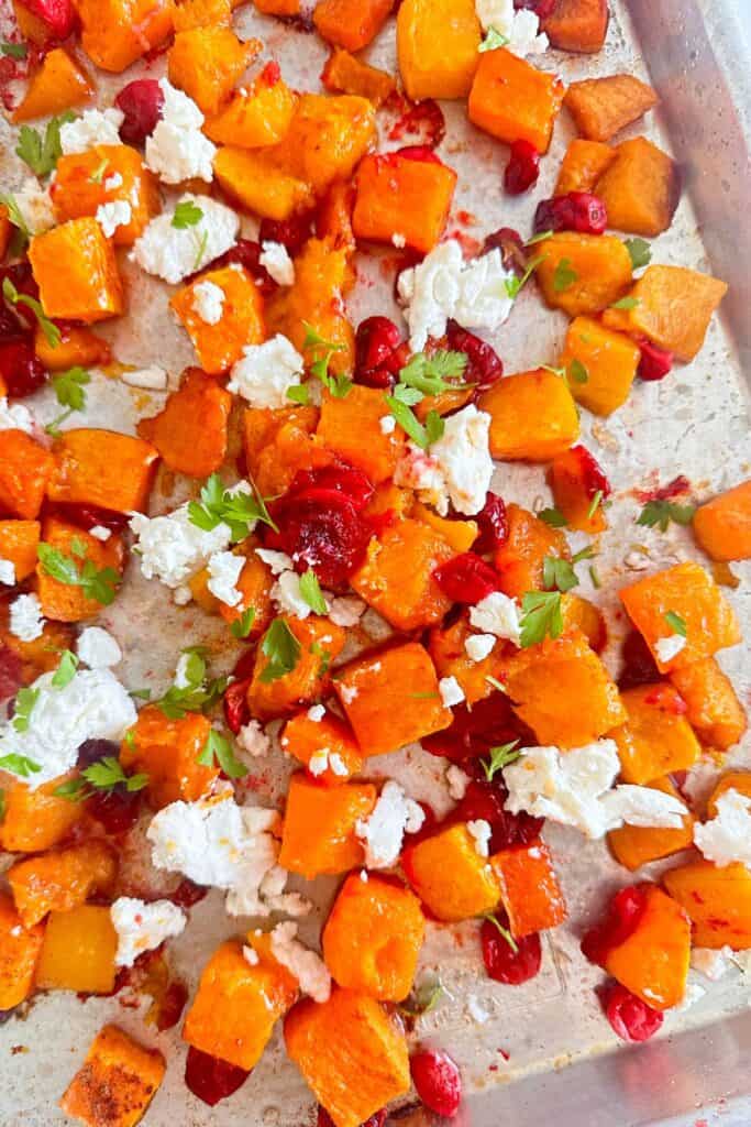 Sheet pan with roasted butternut squash and cranberries topped with goat cheese and fresh parsley.