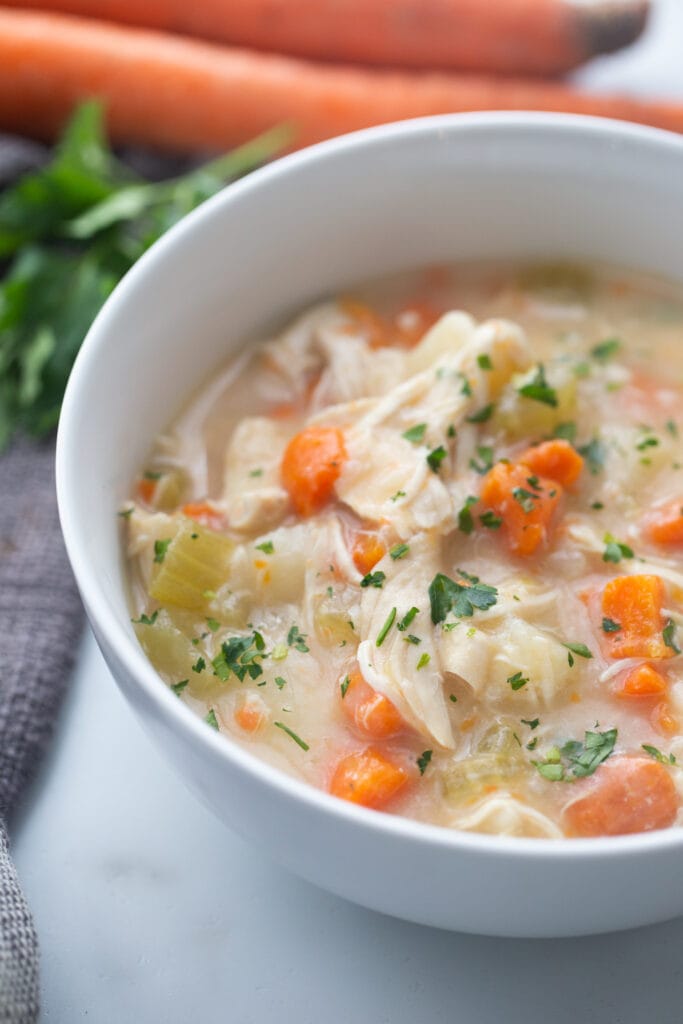 A close up shot of chicken soup shows that it's garnished with freshly cut parsley.