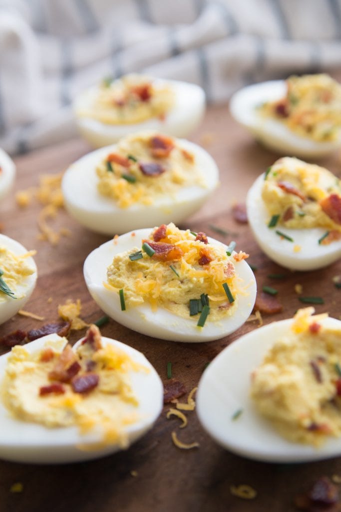 Many Loaded Deviled Eggs topped with bacon bits and chives on a wooden surface- perfect for a healthy brunch recipe!