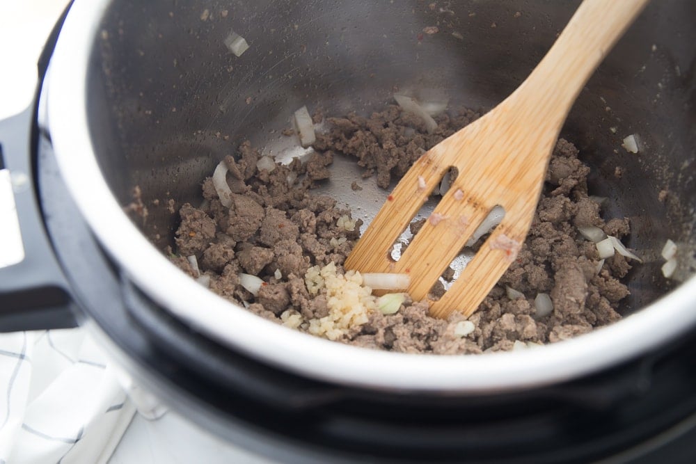 Instant Pot with chicken sausage, onions, and garlic sauteing. A wooden spoon is stirring